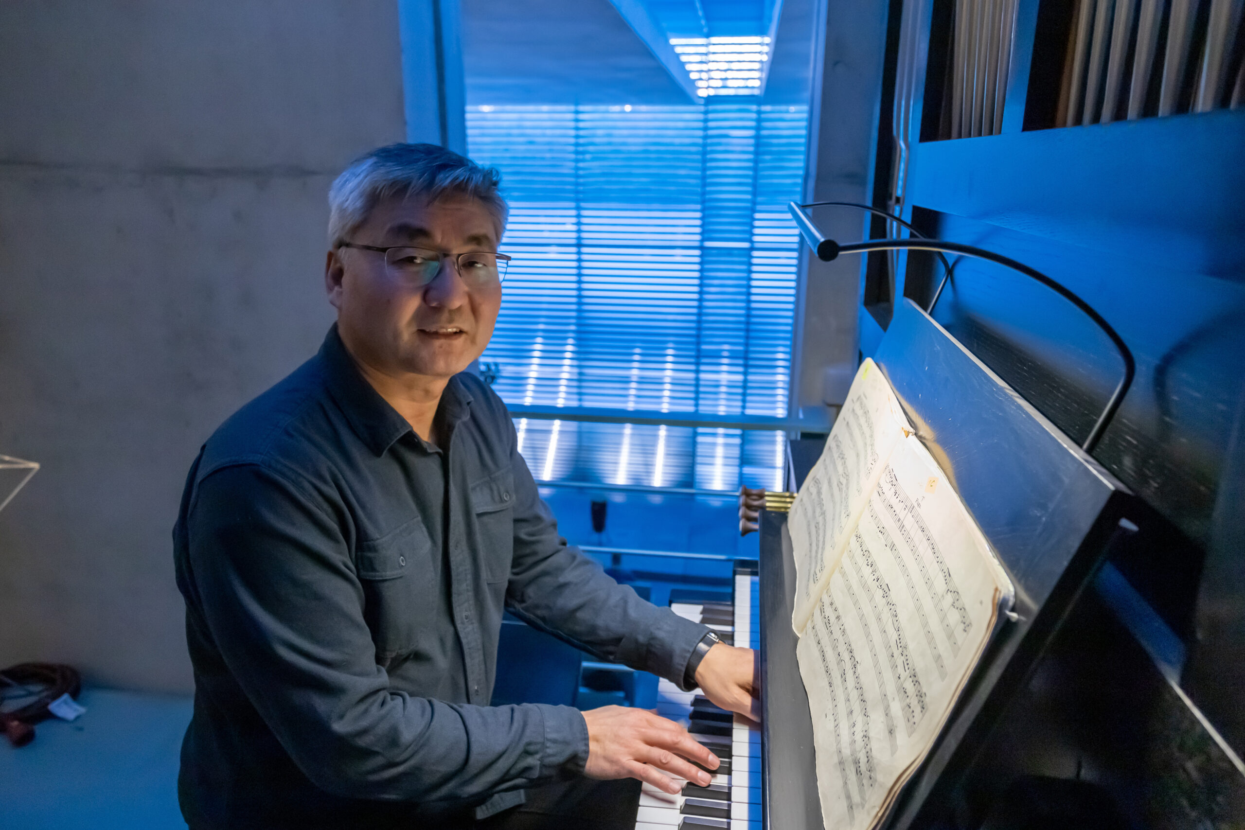 Person sitzt an einer Orgel, blickt zur Kamera und spielt nach Noten
